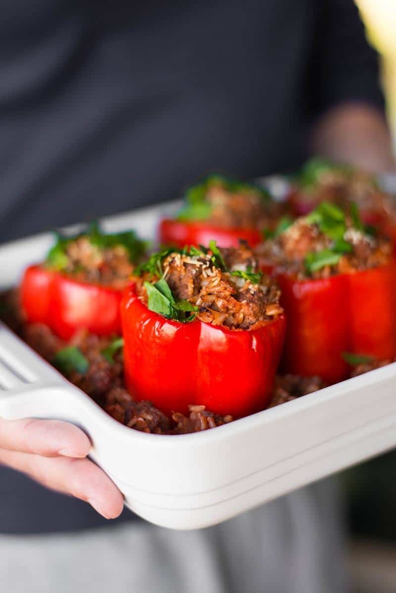 Man holding casserole dish filled with baked stuffed peppers, fresh from the oven, and topped with fresh italian parsley.